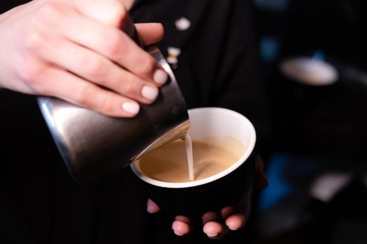 latte art by barista. pouring milk in coffee. dark coffee house.