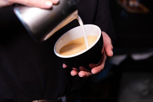 latte art by barista. pouring milk in coffee. dark coffee house.