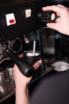 Process of preparing milk foam for cappuccino or latte, heating and whipping. Barista steaming milk in the pitcher