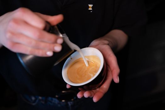 Barista pouring latte foam on coffee, espresso. creating a perfect latte art. dark colours, coffee house.