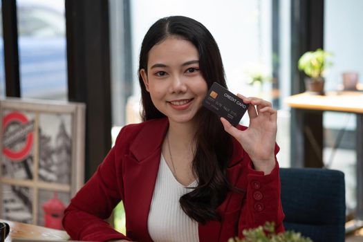 Charming asian woman showing credit card looking on camera. Online banking shopping concept.