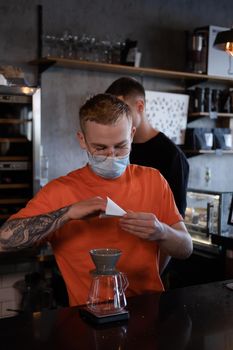 blonde guy in orange t-shirt preparing Alternative coffee brewing: chemex in modern loft coffee shop.