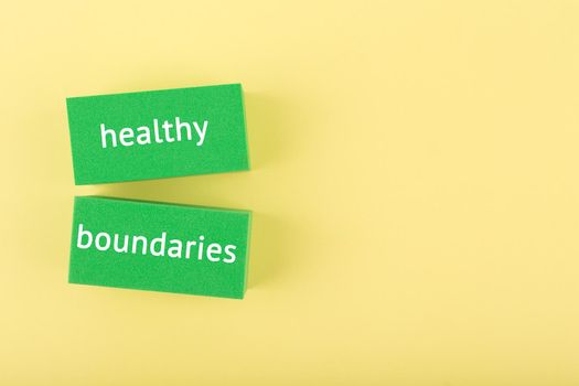 Minimal simple flat lay with green rectangle with written healthy boundaries text on bright yellow background with copy space. Concept of world mental health day, psycology, mental health assessment and awareness