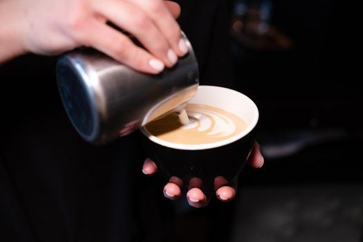 latte art by barista. pouring milk in coffee. dark coffee house.