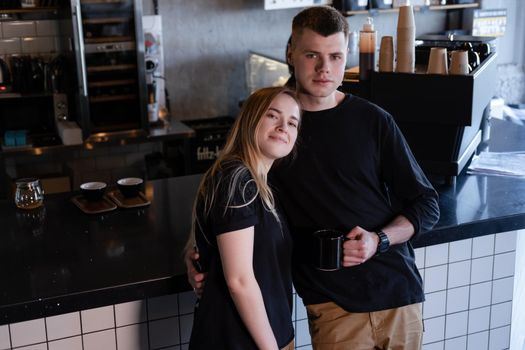 happy married couple in identical clothes family look - cafe owners or workers - in modern coffee shop. family business. loft cafe.