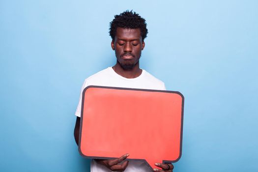 Portrait of young adult holding blank board for communication. Person showing red speech bubble to camera, sign used for written messages and conversation. Man with space for expression