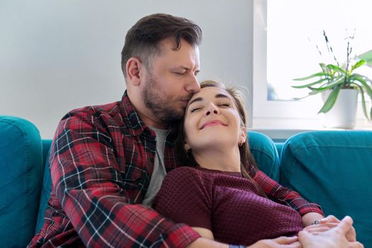 Happy middle-aged couple embracing at home on the couch. Family, happiness, love, relationships, kiss, people 40 years old concept