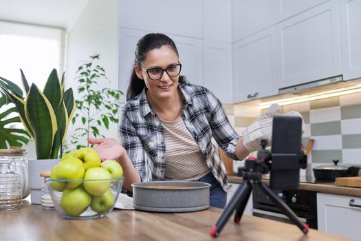 A culinary blog, a female recording a video of an apple pie recipe on a smartphone at home in the kitchen. Blogging, vlog, technology, lifestyle, hobbies and leisure, people concept