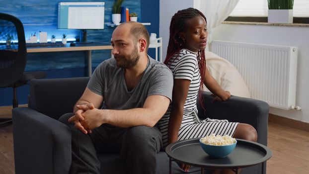 Married interracial people having argument at home sitting on sofa. Irritated multi ethnic couple fighting in living room on couch. Mixed race partners with relationship problems