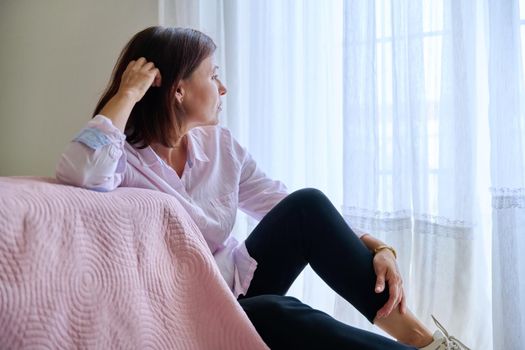 Depression, stress, sadness, mental problems, woman and health. Middle-aged sad upset unhappy female sitting on the floor near the bed at home