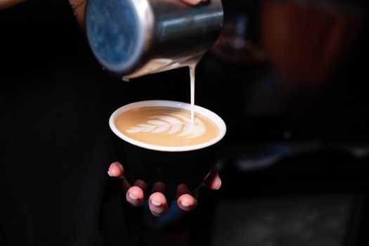 latte art by barista. pouring milk in coffee. dark coffee house.