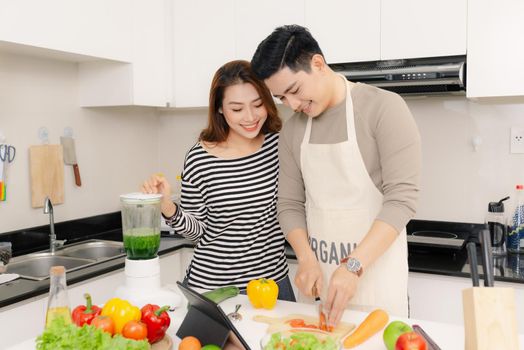 happy young couple have fun in modern kitchen indoor while preparing fresh fruits and vegetables food salad