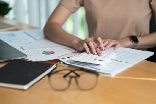 Close up Business woman using calculator and laptop for do math finance on wooden desk in office and business working background, tax, accounting, statistics and analytic research concept