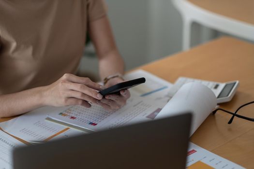 Businesswoman analyzing financial data from paperwork monthly report with smart phone and laptop computer.