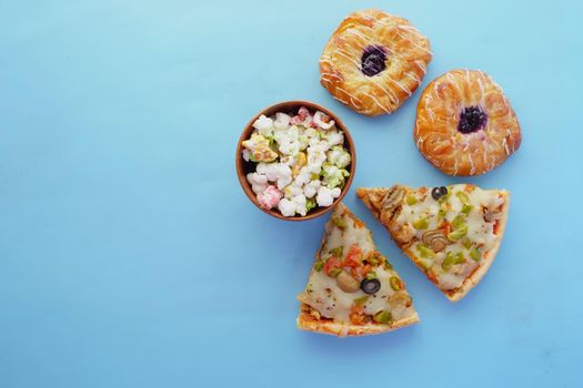 Slice of cheese pizza on a plate , donuts and popcorn on blue .