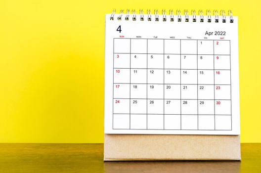 The April 2022 desk calendar with yellow background on the wooden table.