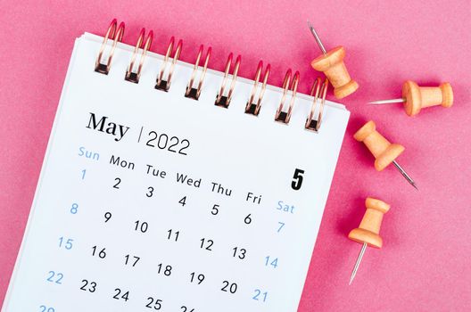 May 2022 desk calendar with wooden pin on pink background.