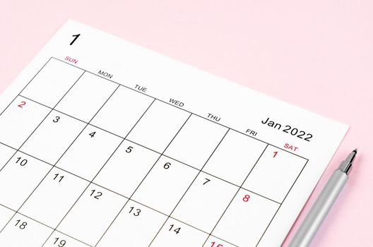 Close up January 2022 calendar sheet with pen on pink background.