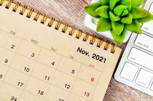 November 2021 desk calendar with keyboard computer on wooden background.
