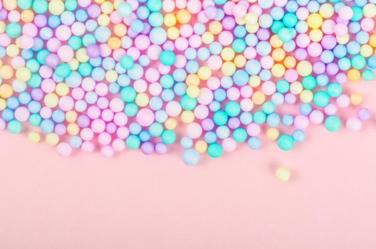 Foam beads of various colors brightly colored on pink pastel background with empty space.