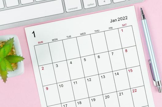 The january 2022 calendar sheet with keyboard computer on pink background.