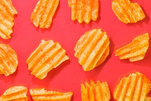 Ribbed potatoes snack with pepper on red background. Ridged potato chips on red background. Set of potato chips. Flat lay. Close-up.