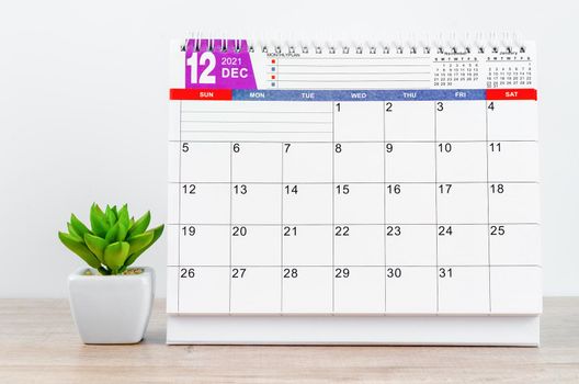 December 2021 desk calendar with plant in pot on wooden table.