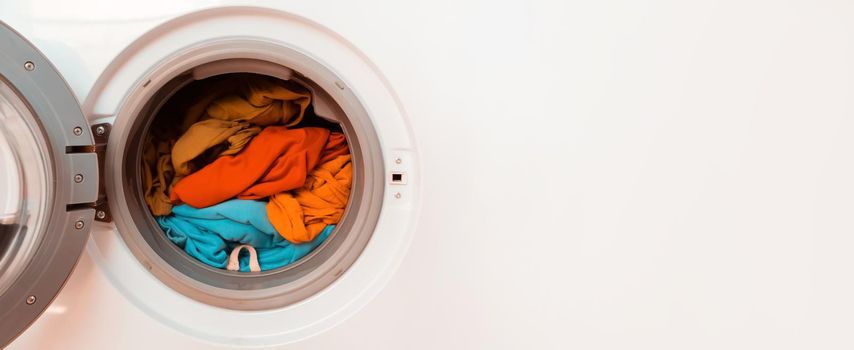 Washing machine with open door and bright colored clothes inside, banner with copy space close-up.