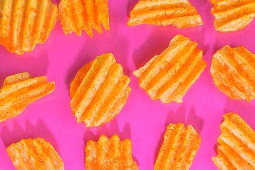 Ribbed potatoes snack with pepper on pink background. Ridged potato chips on pink background. Set of potato chips. Flat lay. Close-up.