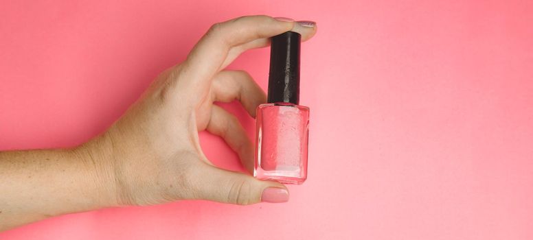 Nail polish in a woman's hand copy space. Article about manicure. Gel polish. Hand care . Pink background