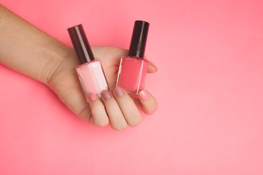 Nail polish in a woman's hand copy space. Article about manicure. Gel polish. Hand care . Pink background