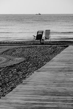 Lonely beach chairs on the shore and wooden walkway to the Levante Beach in Spain