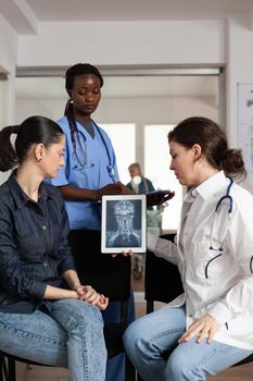 Specialist radiologist doctor analyzing clinical radiography with woman patient during medical appointment in hospital waiting room. African american nurse writing heathcare treatment on clipboard