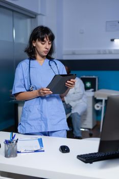 Woman nurse looking at digital tablet working late at night. Medical assistant holding modern gagdet with technology for healthcare system and medical practice, doing overtime work at office.