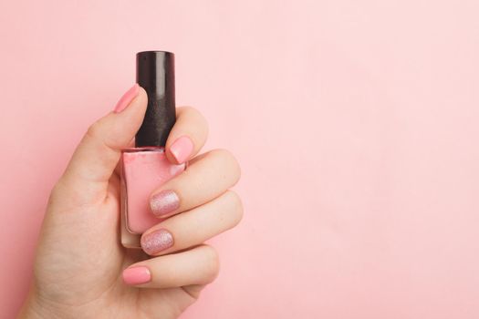 Nail polish in a woman's hand copy space. Article about manicure. Gel polish. Hand care . Pink background