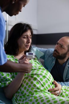 Close up of pregnant person with painful contractions holding hand of nurse and man in hospital ward. Young woman getting into labor while having medical assistance at facility
