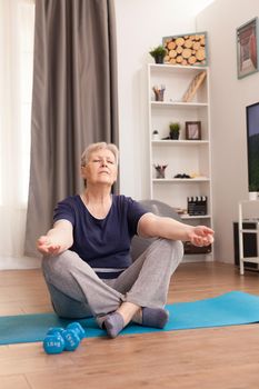 Aged woman practicing yoga at home for a healty life. Old person pensioner online internet exercise training at home sport activity with dumbbell, resistance band, swiss ball at elderly retirement age