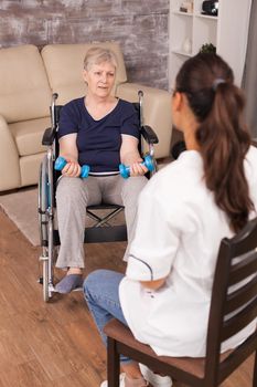 Woman in wheelchair having a conversation with nurseNurse explaining dumbbell exercises Disabled handicapped old person recovering professional help nurse, nursing retirement home treatment and rehabilitation.