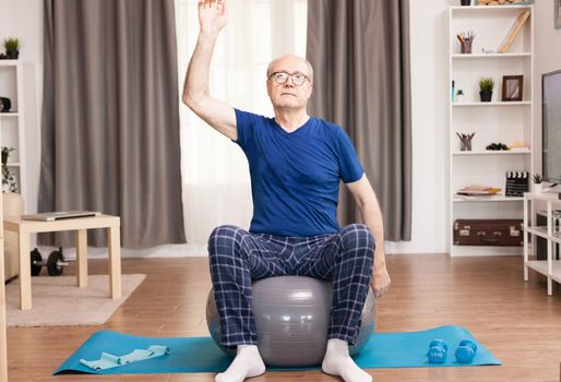 Pensioner doing exercise at home using swiss ball. Old person pensioner online internet exercise training at home sport activity with dumbbell, resistance band, swiss ball at elderly retirement age.