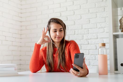 Social media. Young caucasian woman wearing earphones chatting on mobile showing okay sign