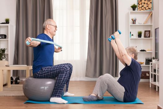 Pensioners doing sport in pajamas with resistance band and dumbbells. Old person healthy lifestyle exercise at home, workout and training, sport activity at home on yoga mat.