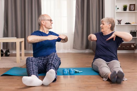 Senior couple doing back exercises sitting on yoga mat. Old person healthy lifestyle exercise at home, workout and training, sport activity at home.