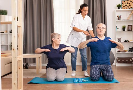 Senior couple enjoying their physical training together assisted by a nurse. Home assistance, physiotherapy, healthy lifestyle for senior old person, training and recovery with professional physiotherapist