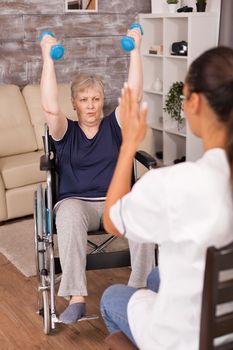 Nurse explaining dumbbell exercises for disabled elderly woman. Handicapped old person recovering professional help nurse, nursing retirement home treatment and rehabilitation