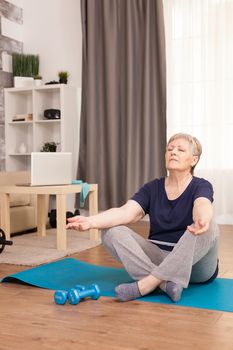 Retired woman relaxing in the living room on yoga mat Old person pensioner online internet exercise training at home sport activity with dumbbell, resistance band, swiss ball at elderly retirement age