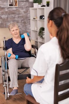 Old lady in wheelchair holding weights for recovery. Disabled handicapped old person recovering professional help nurse, nursing retirement home treatment and rehabilitation