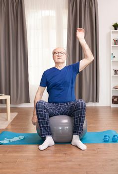 Old man with a healty lifestyle training on living room. Old man training on living room Old person pensioner online internet exercise training at home sport activity with dumbbell, resistance band, swiss ball at elderly retirement age.