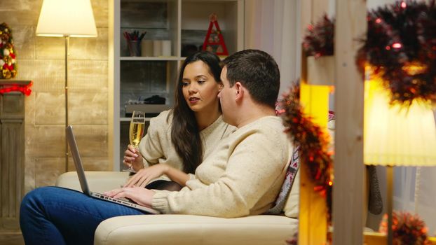 Romantic couple relaxing on couch and browsing on their phones for christmas gifts. Holiday xmas online shopping with credit card via internet, web, searching for season sales. Surprise discount shop purchase in new year eve