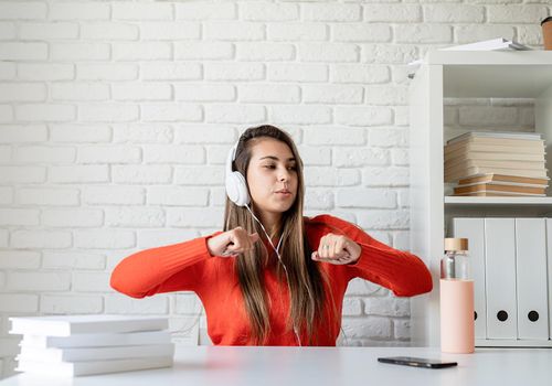 Social media. Young caucasian woman wearing earphones dancing sitting at the table