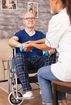 Senior man trying to raise his hand using dumbbells. Disabled handicapped old person with social worker in recovery support therapy physiotherapy healthcare system nursing retirement home